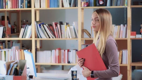 Long-haired blonde holds red folder , smiling with white teeth Stock-Footage 87977014