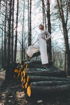 Long haired blonde, standing on the wall of chopped wooden logs, wearing a wh Stock Photos