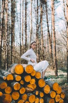 Long haired blonde, standing on the wall of chopped wooden logs, wearing a wh Stock Photos