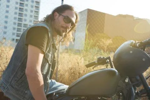 Long-haired brunette guy posing on a black custom motorcycle Stock Photos