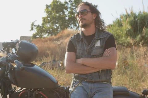 Long-haired brunette guy posing on a black custom motorcycle 스톡 사진