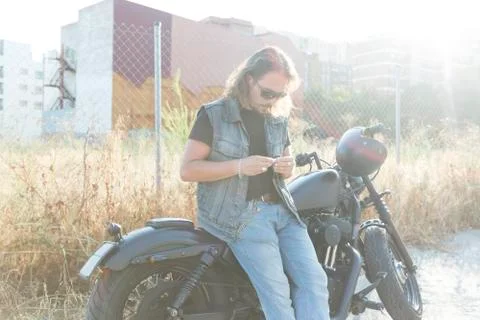 Long-haired brunette guy posing on a black custom motorcycle Stock Photos