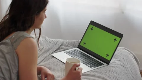 A long-haired brunette lies on a bed with a cup of tea and looks at something Stock Footage 239059547