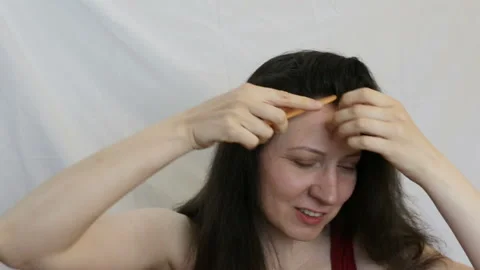 The long-haired brunette makes a parting on her head looking at the camera. Real Stock Footage 92518260