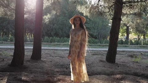 Long haired brunette puts off straw hat walking along park Stock Footage 121064423