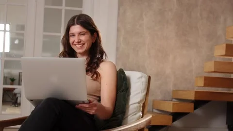 A long-haired brunette waves her hand at the webcam of a laptop and starts to Stock Footage 239323260