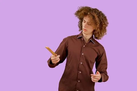 A long-haired curly-haired guy in a brown shirt on a purple background uses a Stock Photos