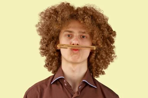 A long-haired curly-haired guy in a brown shirt on a beige background uses a  Stock Photos