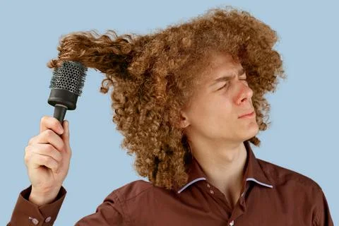 A long-haired curly-haired guy in a brown shirt on a blue background uses a w Stock Photos