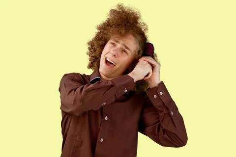 A long-haired curly-haired guy in a brown shirt on a beige background uses a  Stock Photos