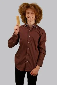 A long-haired curly-haired guy in a brown shirt on a gray background uses a w Stock Photos