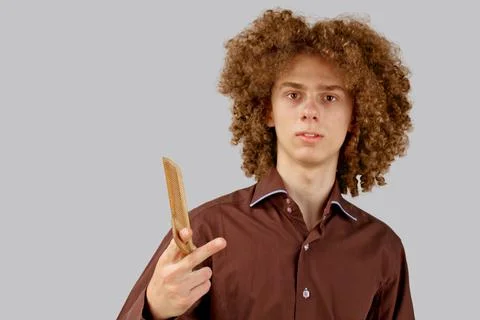 A long-haired curly-haired guy in a brown shirt on a gray background uses a w Stock Photos