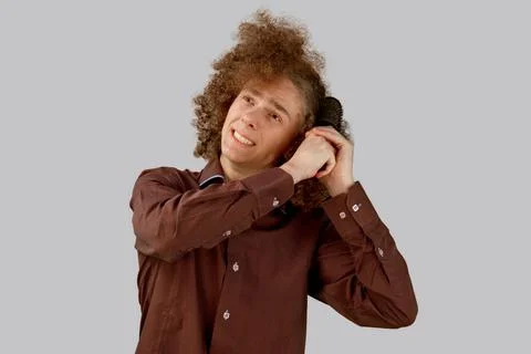 A long-haired curly-haired guy in a brown shirt on a gray background uses a m Stock Photos