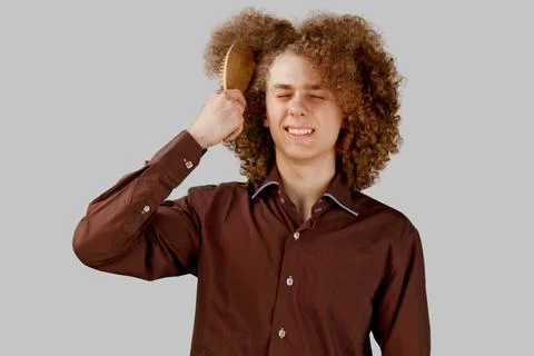 A long-haired curly-haired guy in a brown shirt on a gray background uses a w Stock Photos