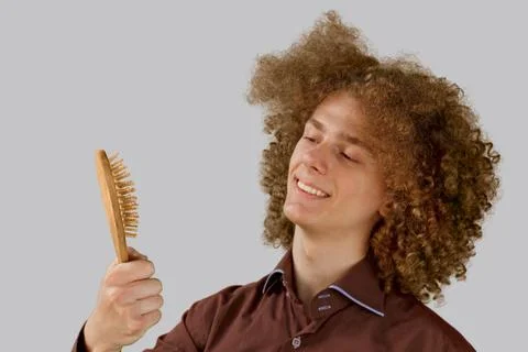 A long-haired curly-haired guy in a brown shirt on a gray background uses a w Stock Photos