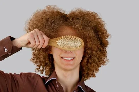 A long-haired curly-haired guy in a brown shirt on a gray background uses a w Stock Photos