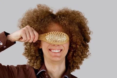 A long-haired curly-haired guy in a brown shirt on a gray background uses a w Stock Photos