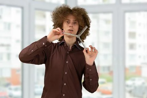 A long-haired curly-haired guy in a brown shirt uses a metal comb. Emotions b Stock Photos