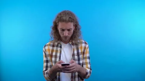 A long-haired curly-haired man with earrings is busy typing a message. a man is Stock Footage 137422960