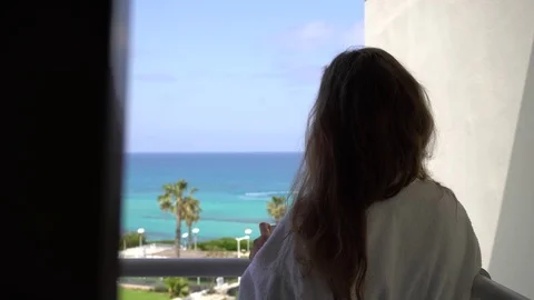 Long-haired girl in bathrobe makes a photo of sea from a hotel balcony using her Stock Footage