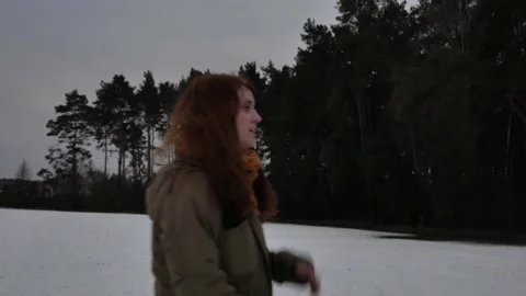 Long haired girl taking off hat and picking up stick on snowy field in winter Stock Footage 143394934