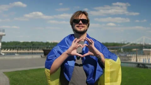 Long-haired guy in black shades wearing blue, yellow flag showing heart symbol 스톡 동영상 197638181