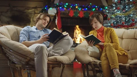 Long haired handsome man and woman reading books on Christmas Stock Footage 100189611