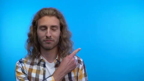 Long-haired happy man points his finger above him. Video on isolated blue Stock Footage 138028602