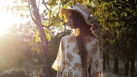 Long haired lady in yellow straw hat stands near green tree Stock Footage 121063129