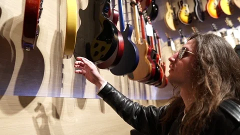 Long Haired Man with Leather Jacket checking selecting guitars in store 2 Stock Footage 124671897