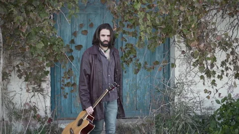 Long haired man looking at the camera while holding a guitar in slow motion Stock Footage 205383563