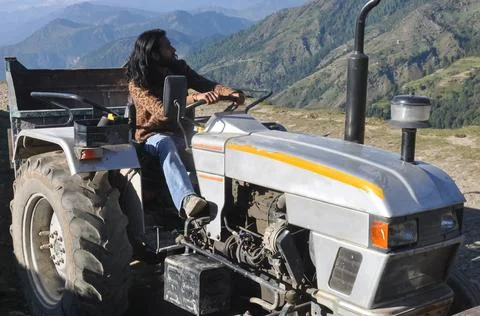 A long haired man looking sideways while driving an old tractor in hilly area  Stock Photos