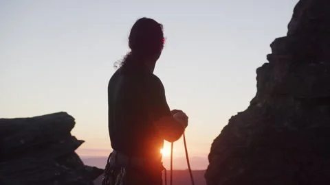 A long haired man setting up a rope for rock climbing at sunset Stock Footage 264139472