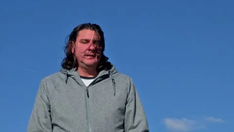 Long-haired man standing against a clear blue sky Stock Footage 326430775