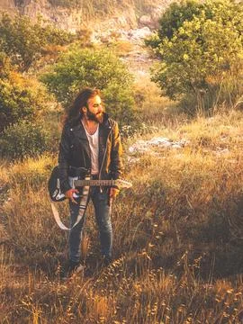 Long haired man walking around with his guitar Stock Photos