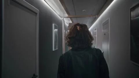 A long-haired man is walking down the corridor of a hotel floor. He is wearing a Stock Footage 252273854
