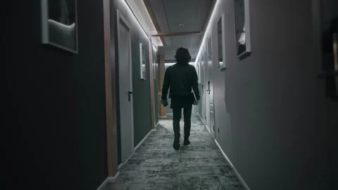 A long-haired man is walking down the corridor of a hotel floor. He is wearing Stock Footage 252274161