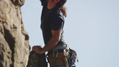 Long-haired rock climber holding onto a rock and climbing Stock Footage 264138524