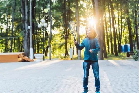 A long-haired school-age boy in jeans and a warm sweater plays a badminton Stock Photos