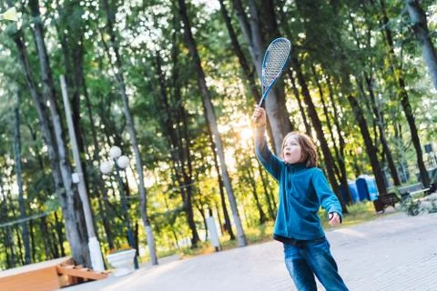 A long-haired school-age boy in jeans and a warm sweater plays a badminton Stock Photos