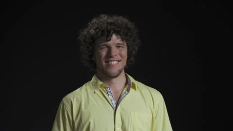 Long haired young guy smile in a silly way and wiggles isolated against a black Stock Footage 143617786