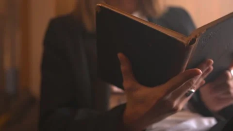 Long haired young man in black suit reads on windowsill aged book in black cover Stock Footage 198027010