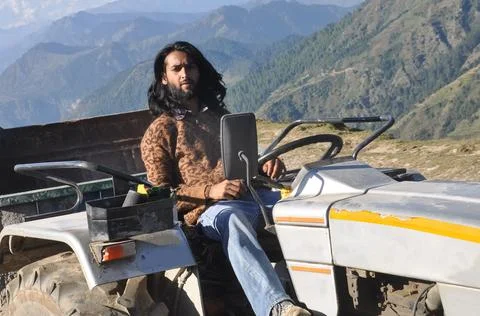 A long haired young men posing with sitting on an old tractor in the mountain  Stock Photos