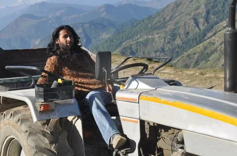 A long haired young men posing with sitting on an old tractor in the mountain  Stock-Fotos