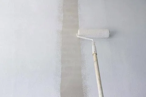 Long handle roller brush applying primer white paint on cement wall backgro.. Photos