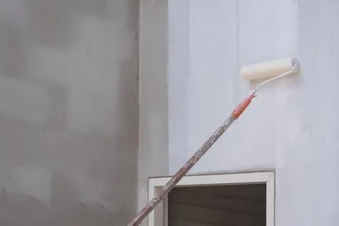 Long handle roller brush applying primer white paint with door frame on cem.. Photos