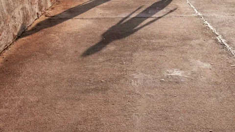 Long human shadows stretch across a sunlit concrete walkway during golden hour. Stock Footage 340945942