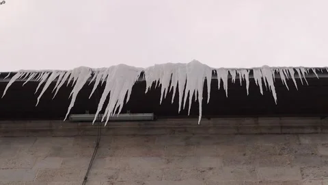 Long icicles hanging from a high building roof that may fall from great height Stock Footage 326297229