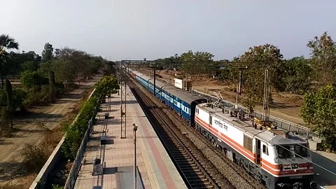 Long Indian Passenger express train crossing scenic Umroli railway station India Stock Footage 140632217