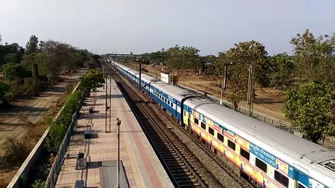 Long Indian Passenger express train crossing scenic Umroli railway station India Stock Footage 140633437